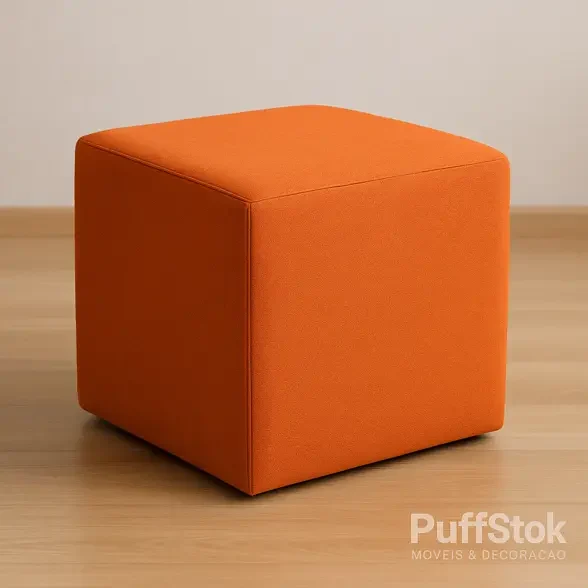 Puff quadrado laranja em tecido, sobre piso de madeira claro, com costuras definidas e acabamento premium.